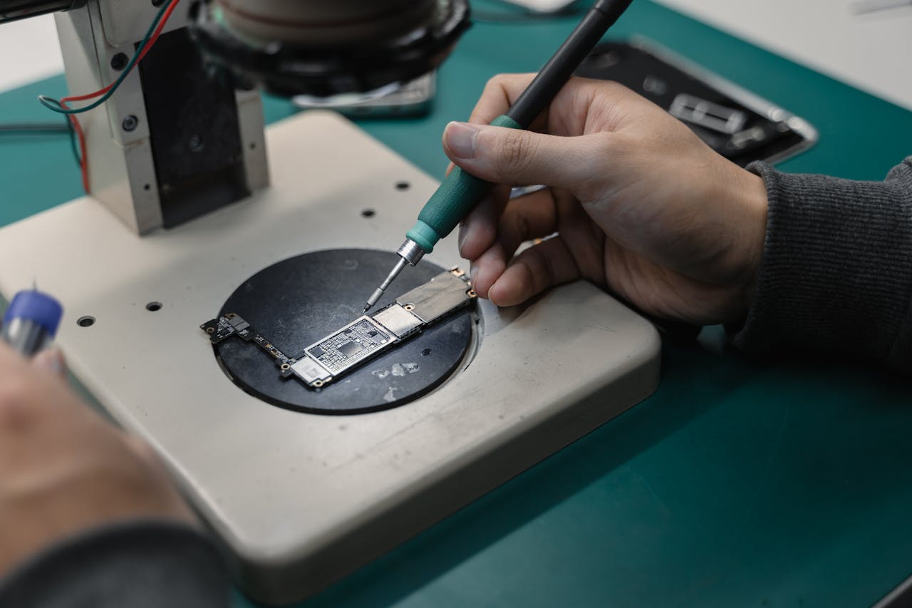 Detail view of hands soldering a circuit board in an electronics workshop.