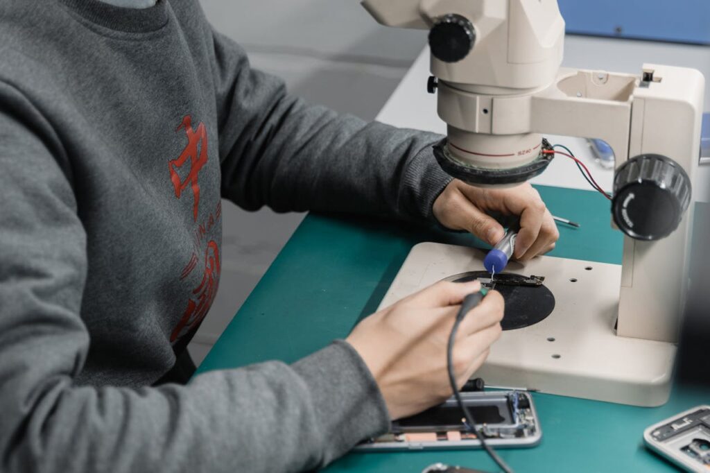 A technician examines a circuit board under a microscope for electronic repair.