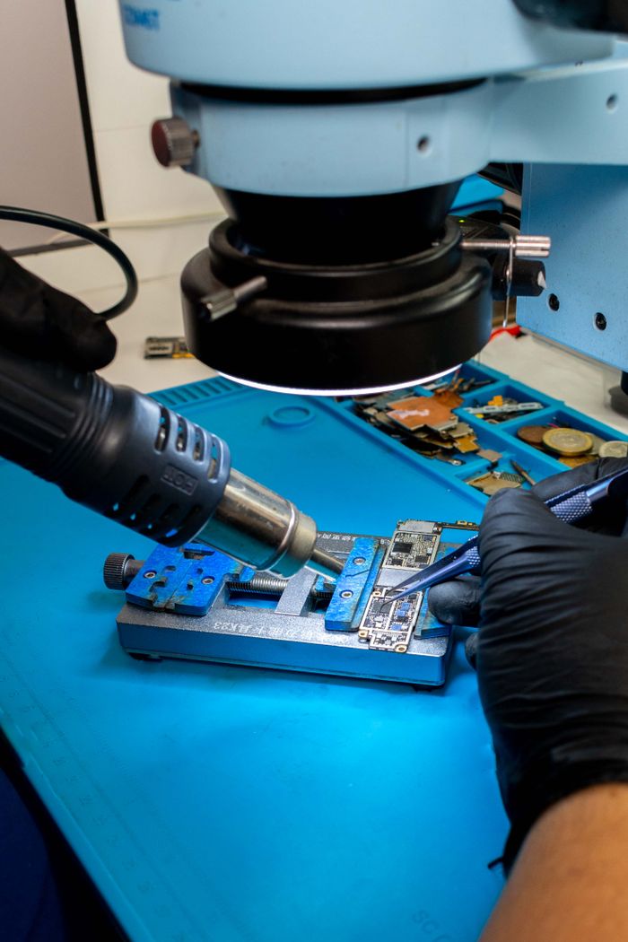 services-04 Close-up of a technician using tools on a circuit board under a microscope.