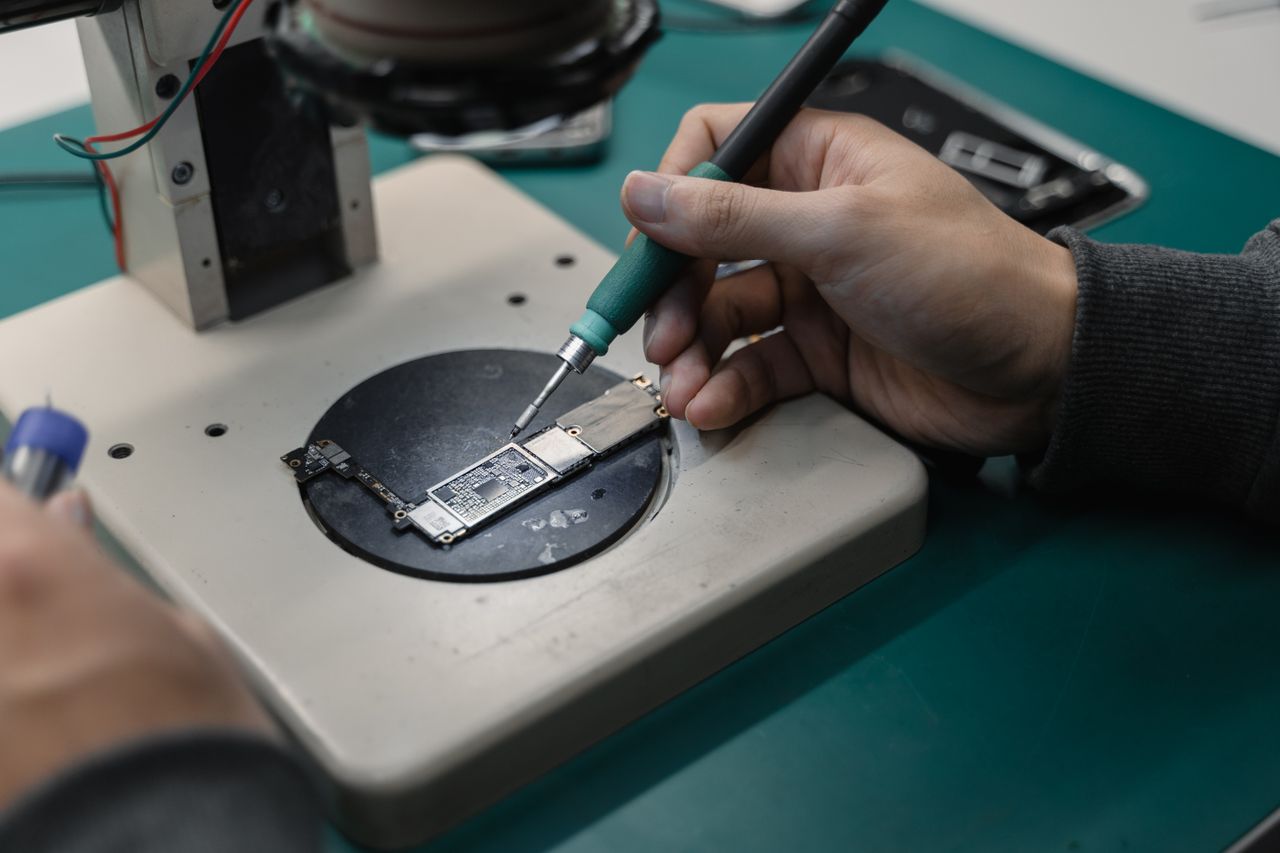 Detail view of hands soldering a circuit board in an electronics workshop.
